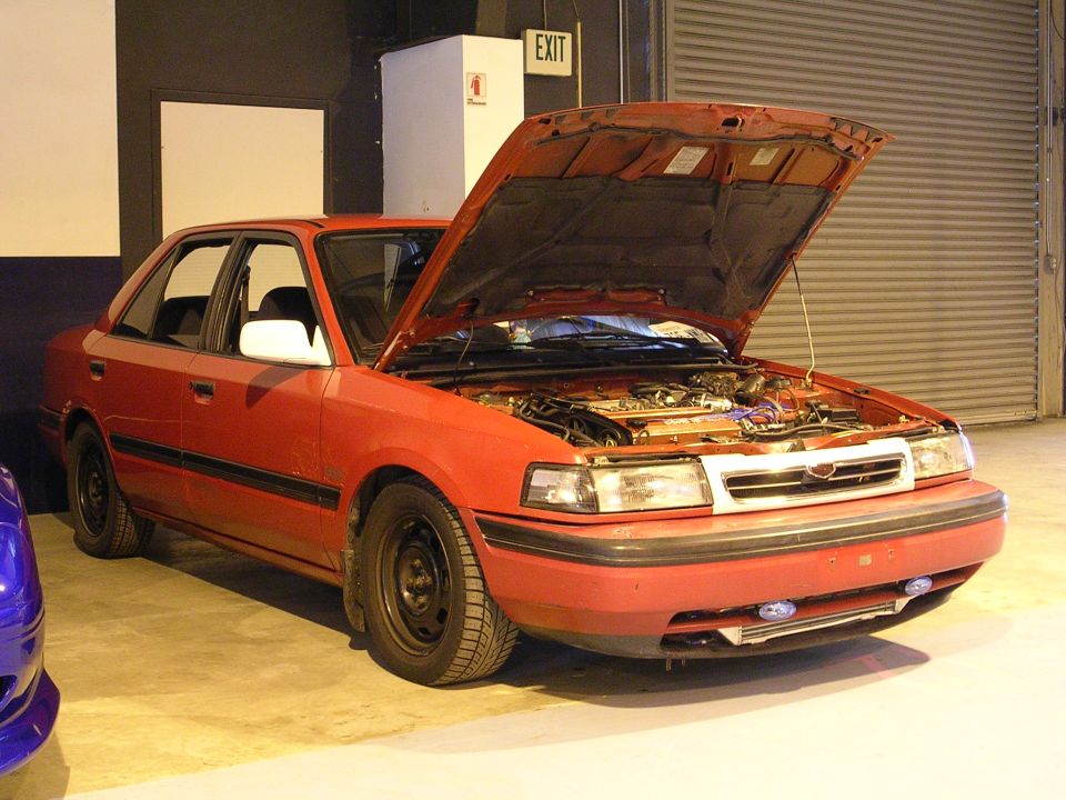 Red sedan with hood open, showing engine bay. Front 3/4 view