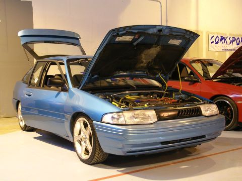 1996 Ford Probe - A blue hatchback is displayed with its hood and trunk open, parked indoors next to a red car.