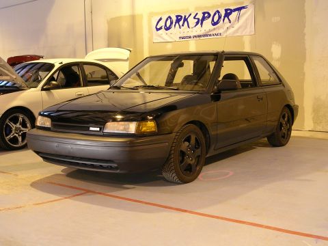1996 Ford Probe - A black hatchback is parked indoors next to another car, with a Corksport banner above.