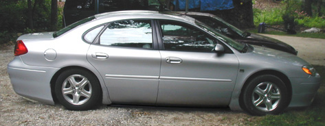 1993 Ford Taurus - A silver sedan is parked next to another vehicle, displaying its side profile with a distinctive rounded body shape.