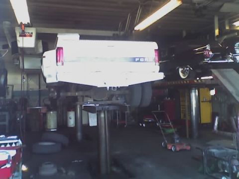 1992 Ford Bronco - A white 1992 Ford F-350 dually pickup truck is shown on a lift in a repair shop, with another vehicle visible above.