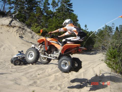 1993 Ford Bronco - An orange ATV takes flight over a sand dune, with a smaller blue ATV visible in the background.