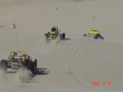 1993 Ford Bronco - Multiple dune buggies race across sandy terrain, kicking up dust as they go.