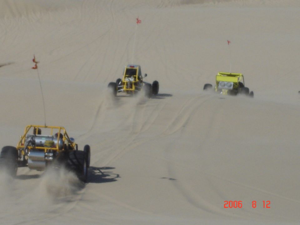 Three yellow dune buggies kicking up sand on a desert dune