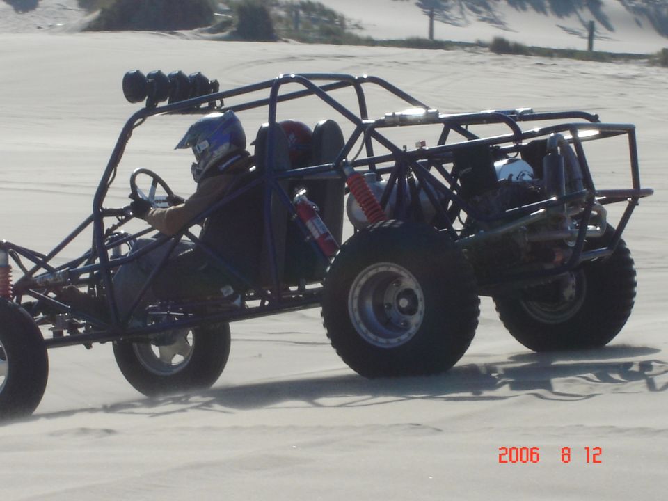 Side view of a dune buggy with a roll cage and large tires on a sandy terrain