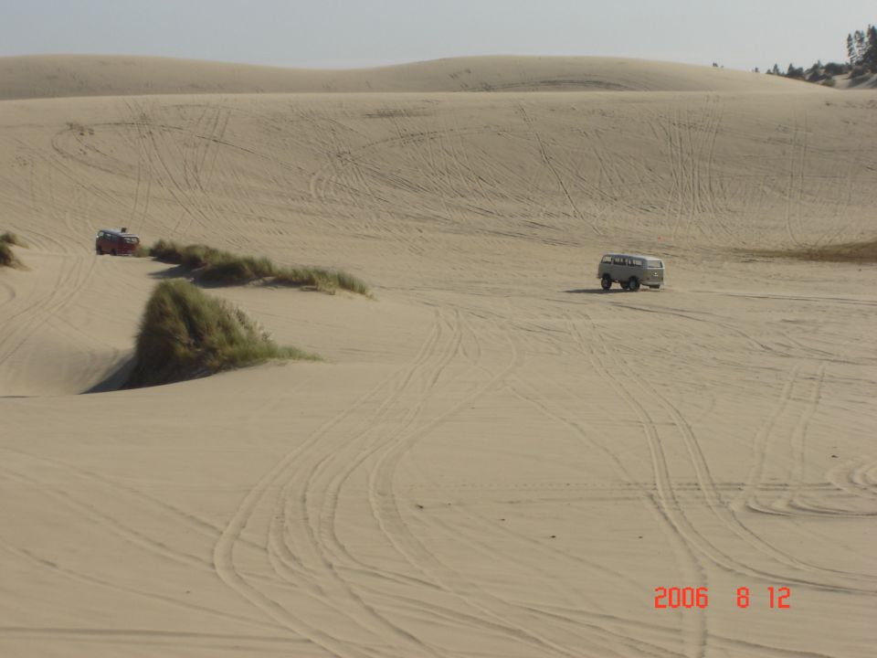 Two vehicles driving on sand dunes, one is a van, the other is a red ATV