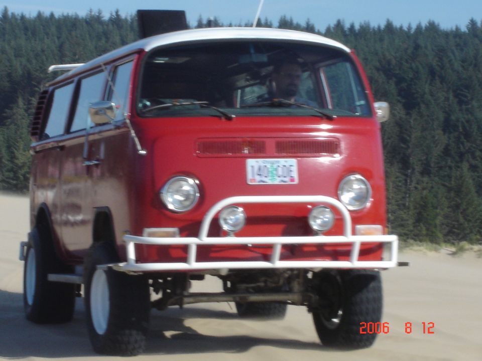 Red Volkswagen Type 2 van with off-road tires and a white roof