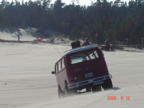 1993 Ford Bronco - Van driving on sand dunes with ATVs in the background.