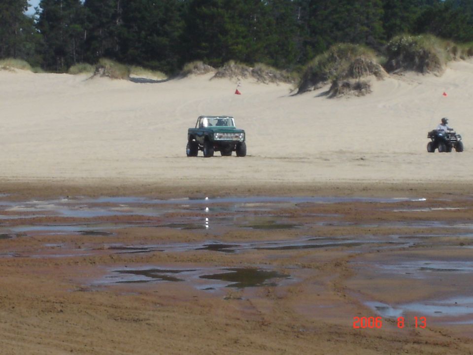 Green SUV and ATV on sand dunes with trees in background