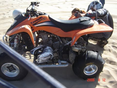 1993 Ford Bronco - An orange Kawasaki ATV is parked on a sandy dune with two people attending to it.