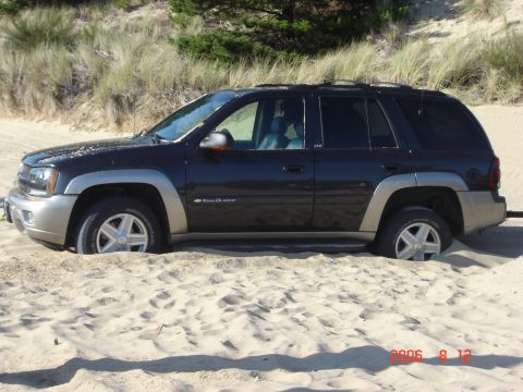 1993 Ford Bronco - This dark SUV is stuck in the sand dunes, with its tires partially buried.