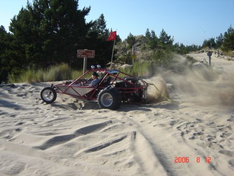 1993 Ford Bronco - A dune buggy navigates sandy terrain, kicking up a cloud of dust under a clear blue sky.