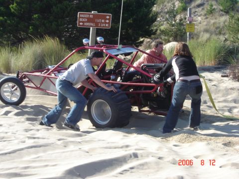 1993 Ford Bronco - People attempt to free a red dune buggy from sand near a signpost.