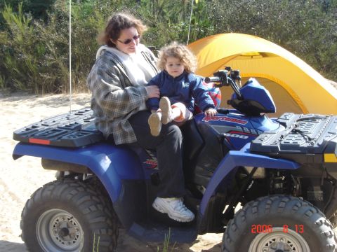 1993 Ford Bronco - A woman and a young child are seated on a blue all-terrain vehicle, with a yellow tent visible in the background.
