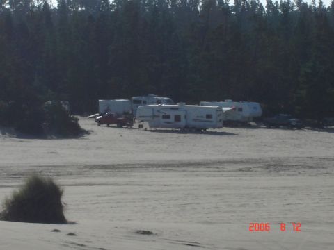 1993 Ford Bronco - A group of recreational vehicles and a pickup truck are parked in a sandy area with a forest in the background.