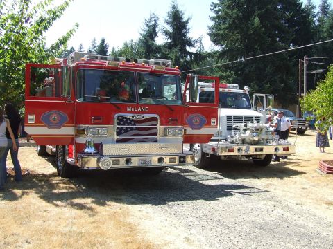 1976 Ford F-150 - Two fire trucks are parked outdoors on a gravel lot with trees in the background.