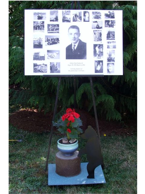 1976 Ford F-150 - Outdoor memorial display board a portrait and various photographs, set against a backdrop of greenery.