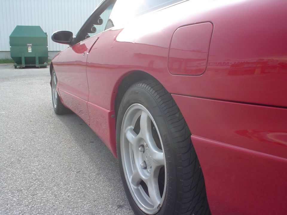 Side view of a red 1996 Ford Probe parked next to a green dumpster