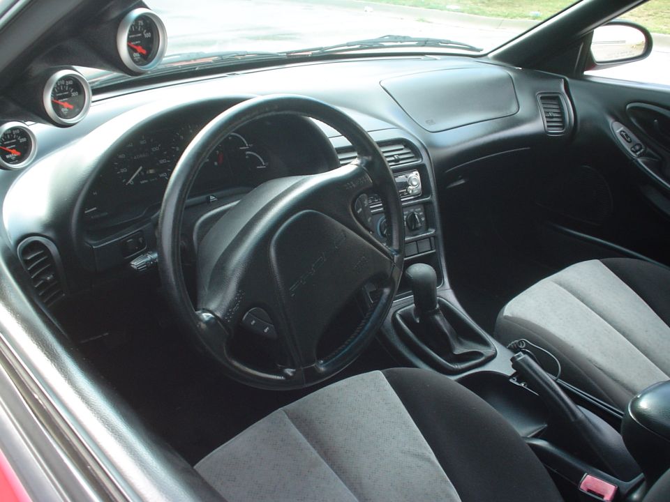 Interior of a 1996 Ford Probe showing dashboard, steering wheel, center console with shifter, and aftermarket gauges
