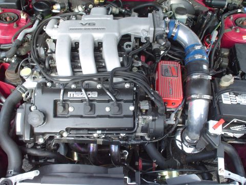 1996 Ford Probe - Engine bay view of a Mazda V6 DOHC 24-valve engine, a red aftermarket ignition module and custom intake piping.