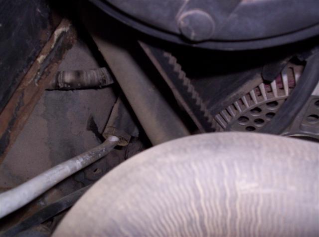 Close-up of engine belt and alternator with hoses and rusty metal