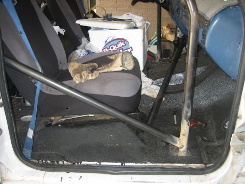 1994 Ford Bronco - The interior of a vehicle is shown, a roll cage, a cooler, and a pair of work gloves resting on the seat.