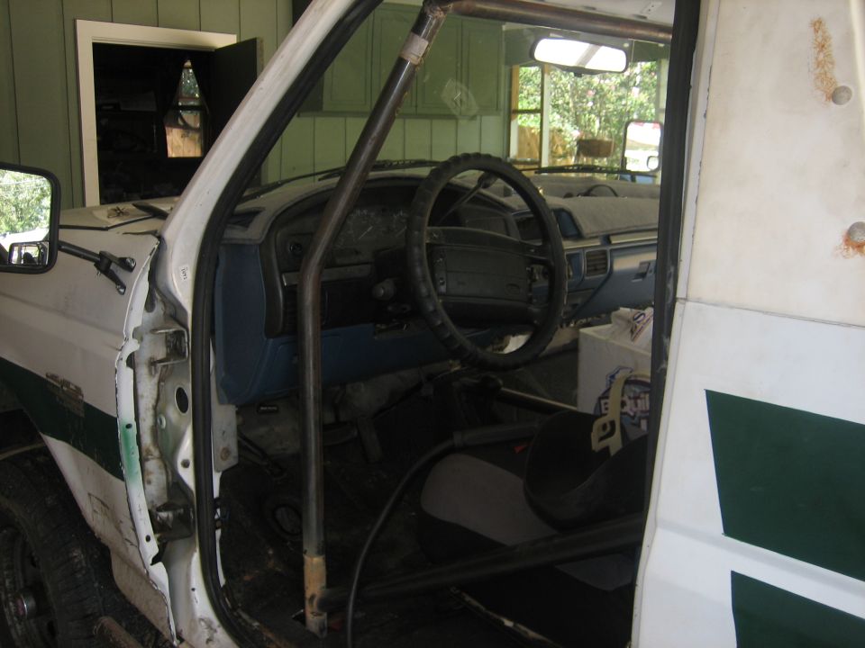 Interior view of a white truck with a roll cage, blue dashboard, and racing seat