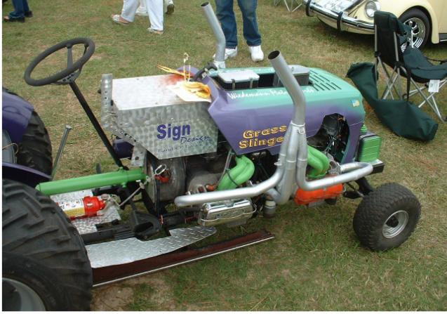 Custom riding mower with dual exhaust pipes, a V8 engine, and 'Grass Slinger' text on the side