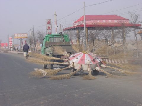 1968 Ford Mustang - A green truck tows a unique street sweeper with numerous brooms attached, seen on a dusty road.