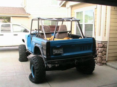 1971 Ford Bronco - Rear view of a modified blue 1971 Ford Bronco with a roll cage and large off-road tires parked in a driveway.