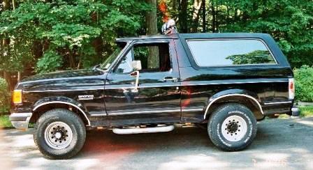 1991 Ford Bronco - This 1991 Ford Bronco is shown from the side, parked outdoors with trees in the background.
