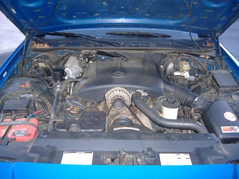 1998 Ford Crown Victoria - The engine bay of a blue 1998 Ford Crown Victoria is visible with the hood raised, revealing the V8 engine components.