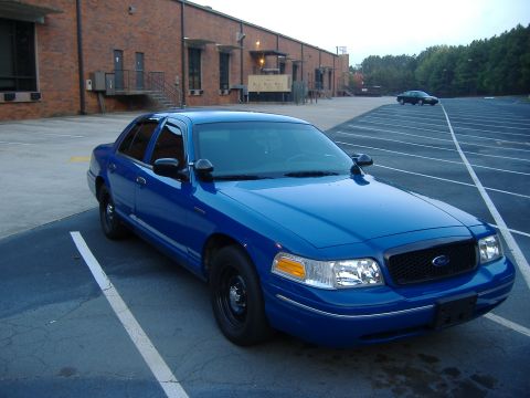 1998 Ford Crown Victoria - A blue sedan is parked in a lot with a brick building in the background and another car in the distance.
