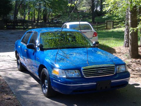 1998 Ford Crown Victoria - A blue sedan with a chrome grille is parked outdoors, with another white car visible in the background.