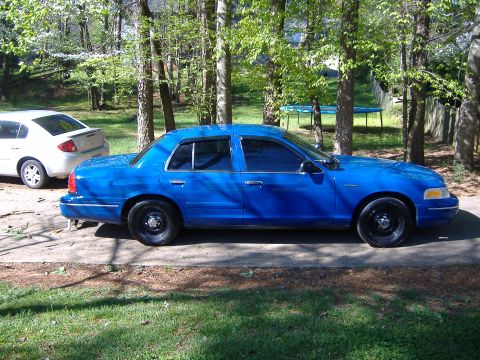 1998 Ford Crown Victoria - Side view of a blue 1998 Ford Crown Victoria sedan parked outdoors with another car visible in the background.