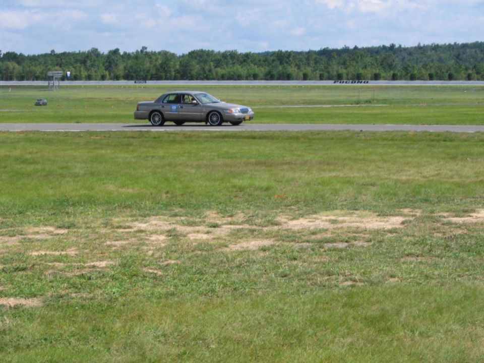 2001 Mercury Grand Marquis driving on a paved track with grassy fields and trees in the background