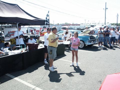2001 Mercury Grand Marquis - An outdoor event with people interacting near a table and a vintage car with its hood open.