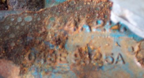 1975 Ford F-150 - A heavily rusted metal component displays stamped alphanumeric identifiers, suggesting it is a vehicle part.
