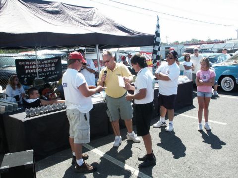 2001 Mercury Grand Marquis - Awards are being presented at a car show event, with a crowd and vehicles in the background.