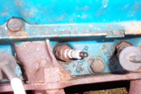 1975 Ford F-150 - Close-up of a spark plug installed in a weathered engine block, showing signs of age and use.