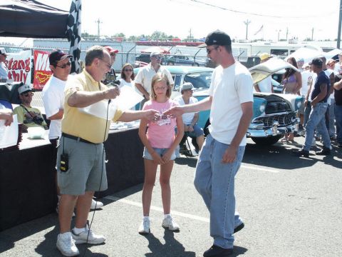 2001 Mercury Grand Marquis - A car show event with people gathered around a table and several vehicles in the background.
