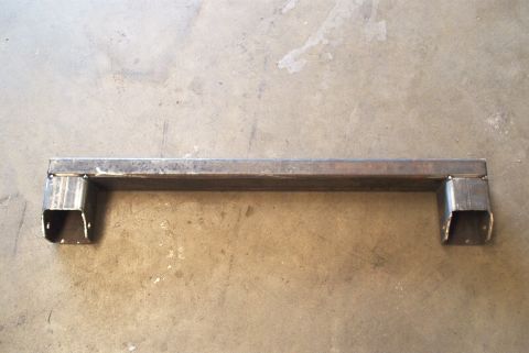 1983 Ford Bronco - This is a metal crossmember part, likely for a vehicle, shown on a concrete surface.