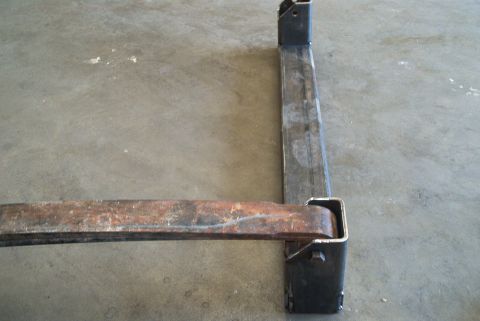 1983 Ford Bronco - A close-up view of a rusty metal crossmember part, likely from a vehicle's chassis, resting on a concrete surface.