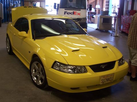 2002 Ford Mustang - A yellow Ford Mustang is parked in a garage with its hood up, and a FedEx truck is visible behind it.