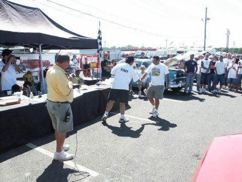 2001 Mercury Grand Marquis - A car show event with attendees and staff near a table, with several vehicles visible in the background under a sunny sky.