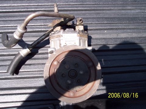 1985 Ford Bronco - An air conditioning compressor part is shown, with hoses connected to its metal body.