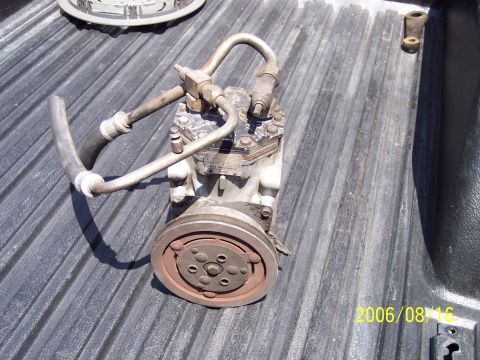 1985 Ford Bronco - An air conditioning compressor with attached hoses and pulley sits on a truck bed.