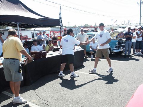 2001 Mercury Grand Marquis - Two men shake hands at an outdoor event, with a vintage car and spectators visible.