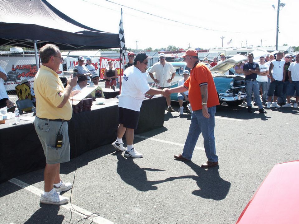Car show award ceremony with people shaking hands and a classic car in the background