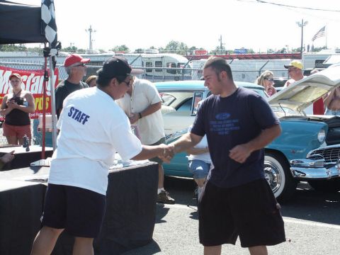 2001 Mercury Grand Marquis - A teal classic car is displayed with its hood open at a car show, while two men shake hands in the foreground.